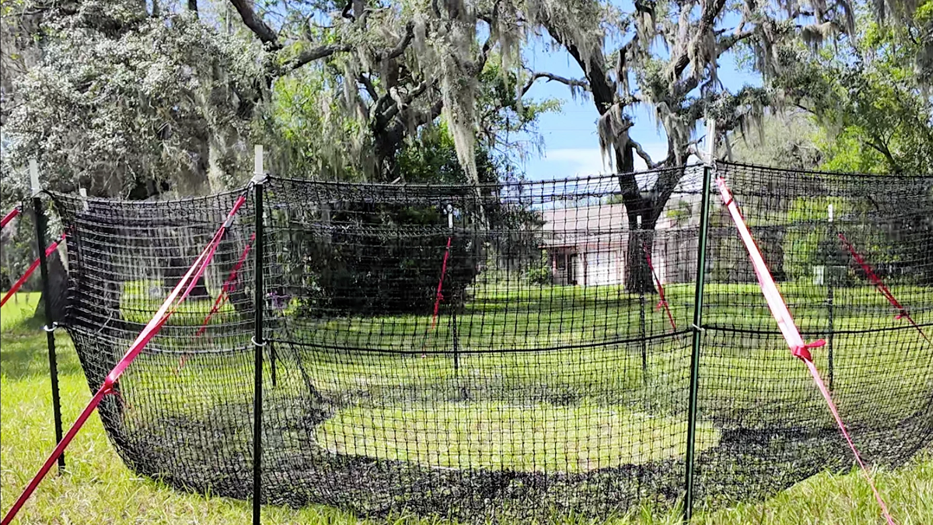 16:9 landscape close view of The P.I.G. Hog Trap™ at ground level with a home in the background, showcasing a complete sounder removal solution designed to help protect homes, property, and surrounding land from feral hog damage.
