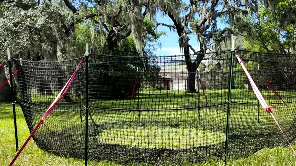 16:9 landscape view of The P.I.G. Hog Trap™ with natural colors and a home in the background, showcasing a feral hog control solution designed to help protect residential property through complete sounder removal.