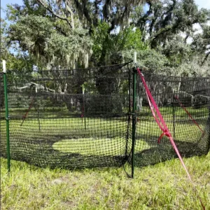 Close view of The P.I.G. Hog Trap™ wild hog trapping system showing bracket strap attachment, support pole, and oak tree in the background for effective feral hog control and complete sounder removal.