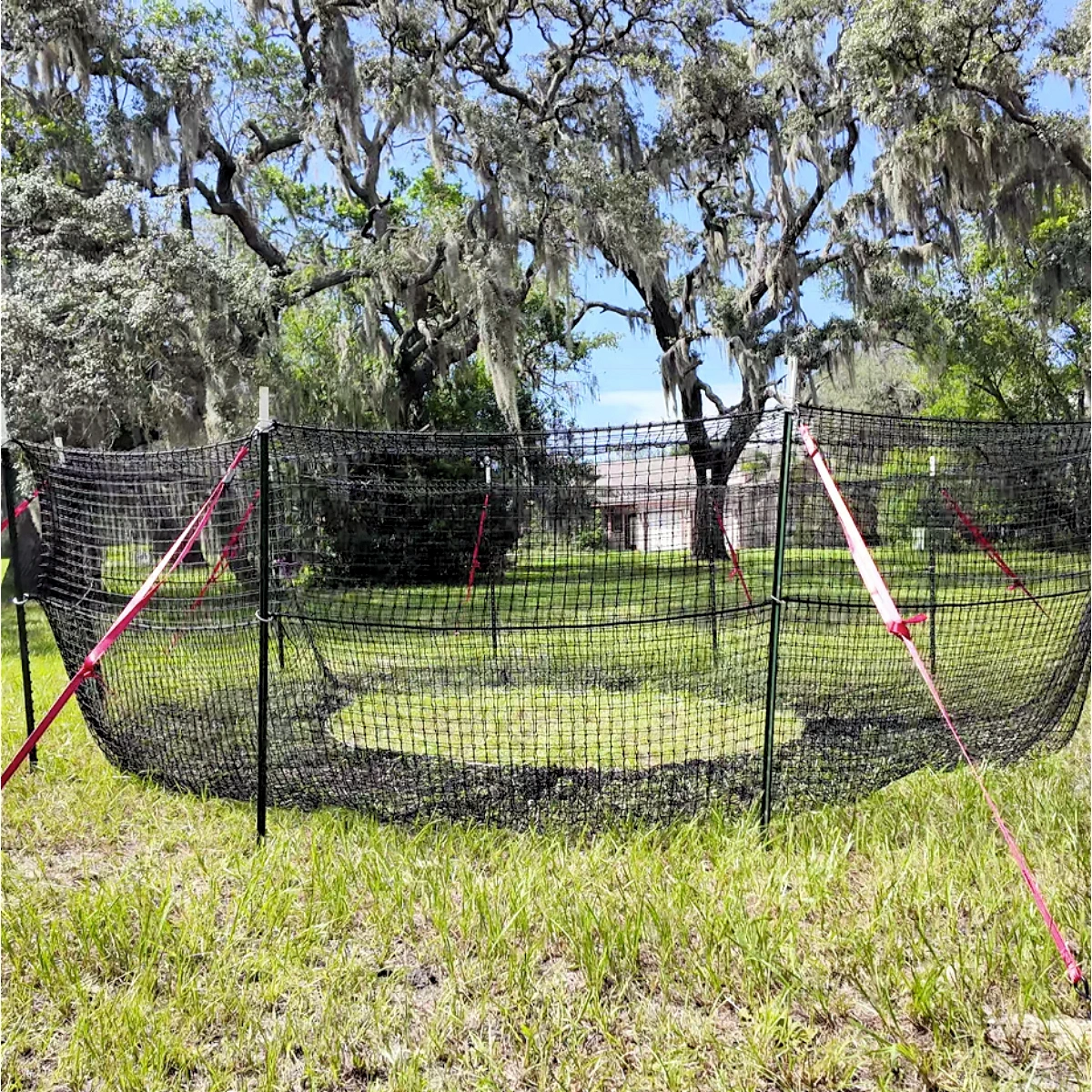 1:1 square centered view of The P.I.G. Hog Trap™ at ground level with a home in the background, showcasing a complete sounder removal system designed to help protect homes, family property, and surrounding land from destructive feral hog activity.